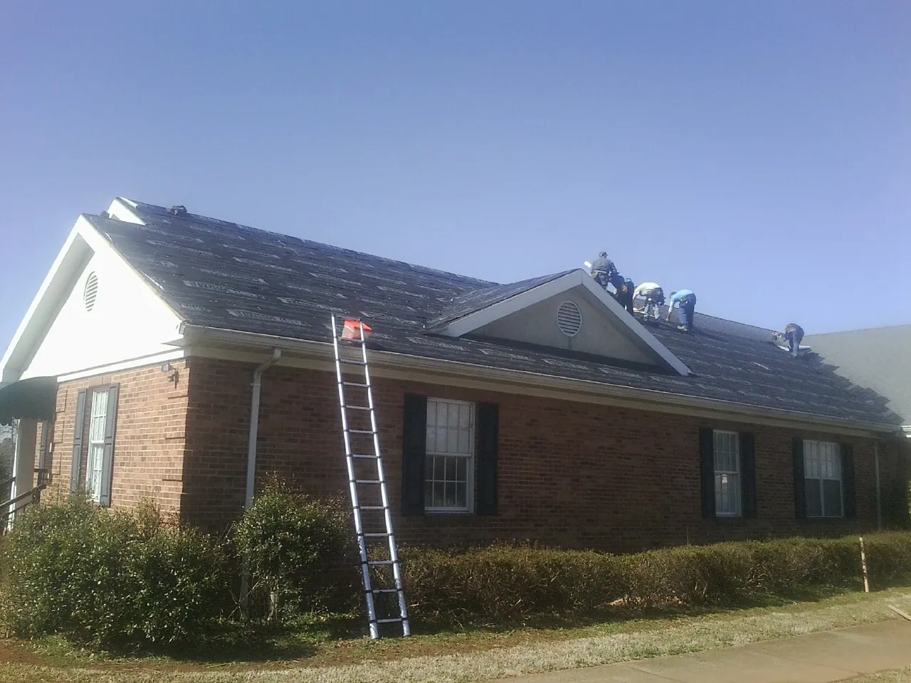 Crew tearing shingles off a brick ranch roof with a ladder set — Metal Roof Repair work by our crew in Pemberton