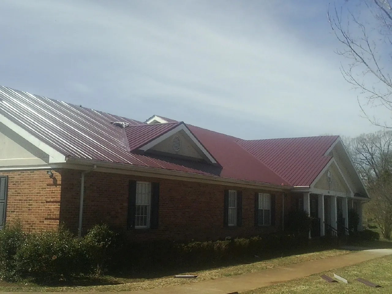 Red metal roof with gabled entries on a long brick building, from a Hail Damage Roof Repair job in Pemberton