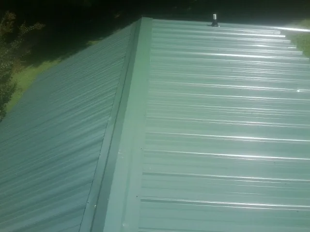 New green metal panels meeting at the ridge of a roof — Flat Roof Repair work by our crew in Pemberton