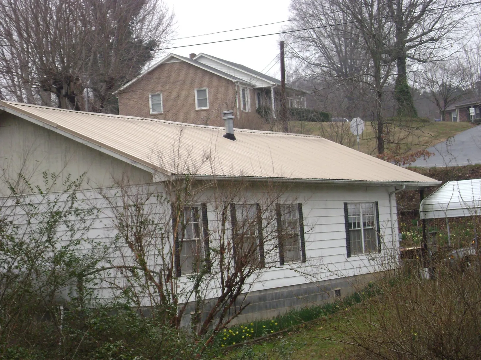 Tan metal roof on a white sided house set into a hillside — Commercial Roofing by Roofing Brothers in Pemberton